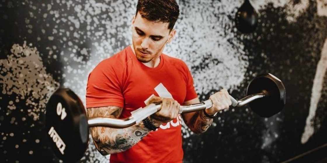Barbell curl mid-rep in the gym, chalk dust in the air